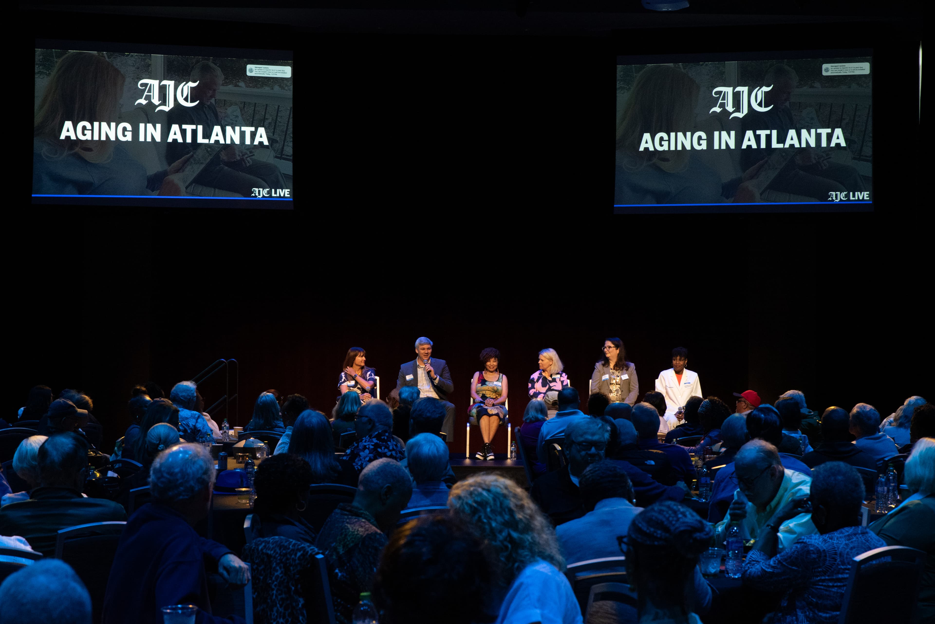 Wide view of the Aging in Atlanta panel at AJC Live, twin screens reading AJC Aging in Atlanta with a packed audience seated below