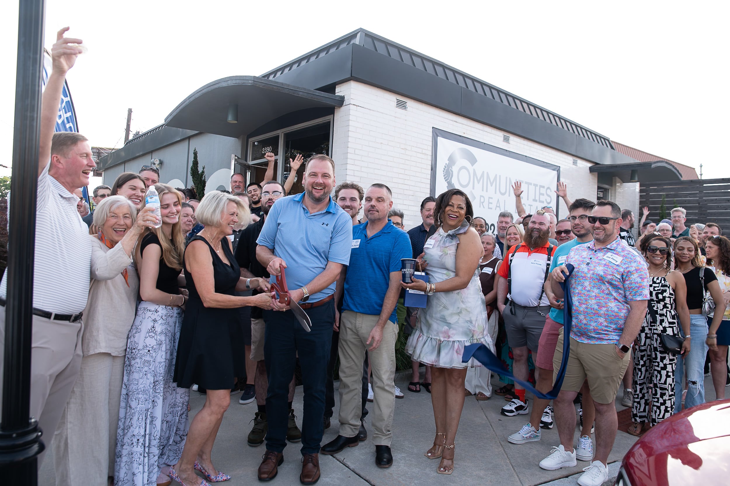 Communities Real Estate ribbon cutting moment with Blake Glover, ceremonial scissors, and the celebrating crowd at the Atlanta grand opening