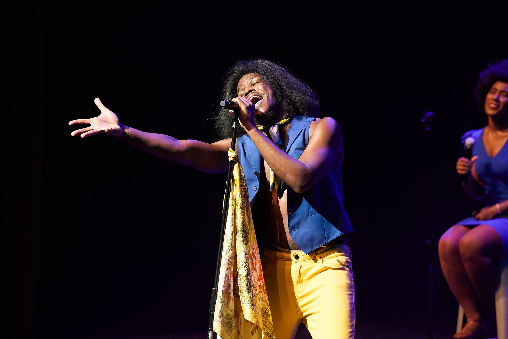 Live performer singing with arm outstretched under dramatic purple and blue stage lighting
