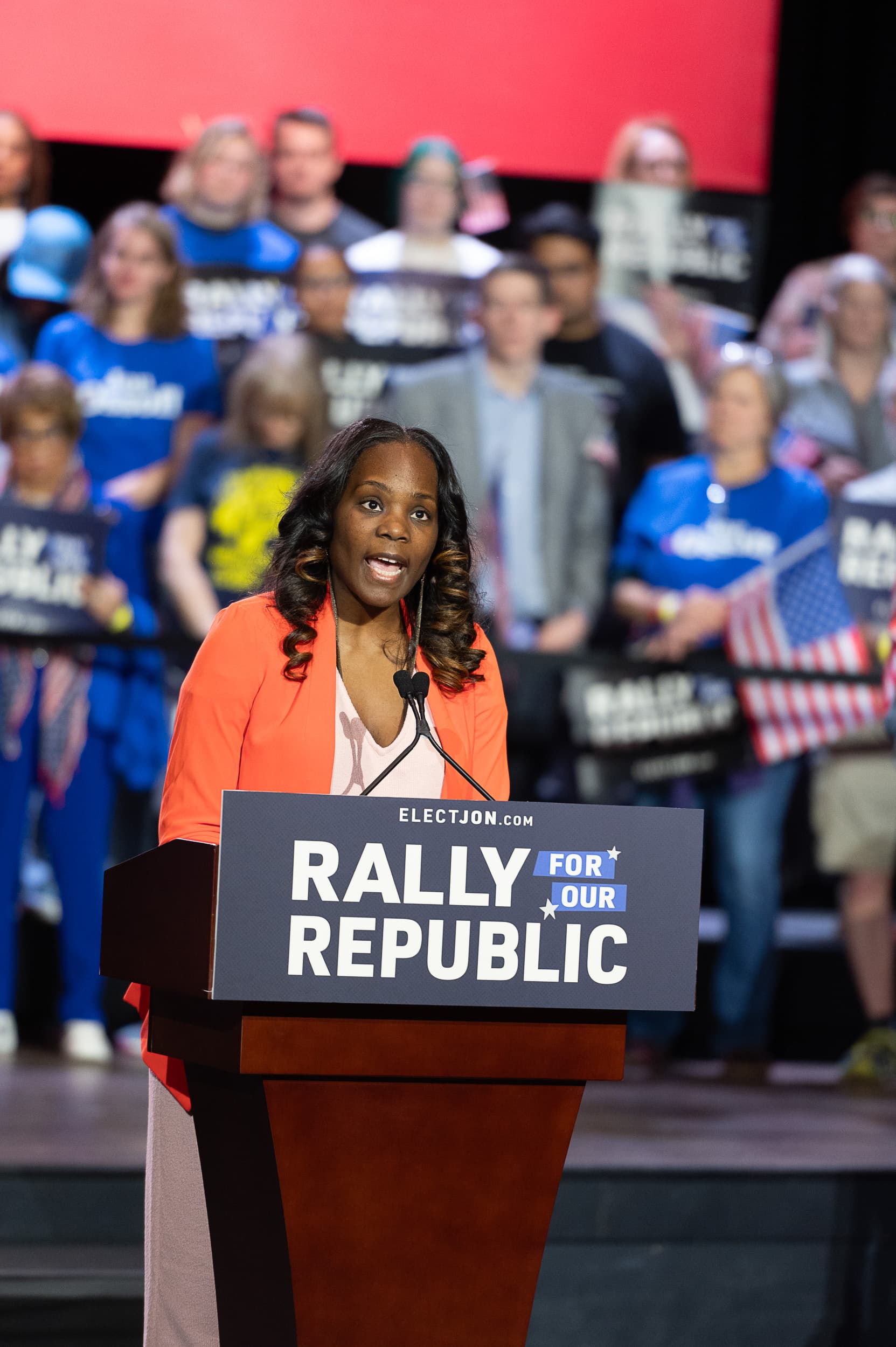 Speaker in orange blazer addressing crowd at large-scale Atlanta event