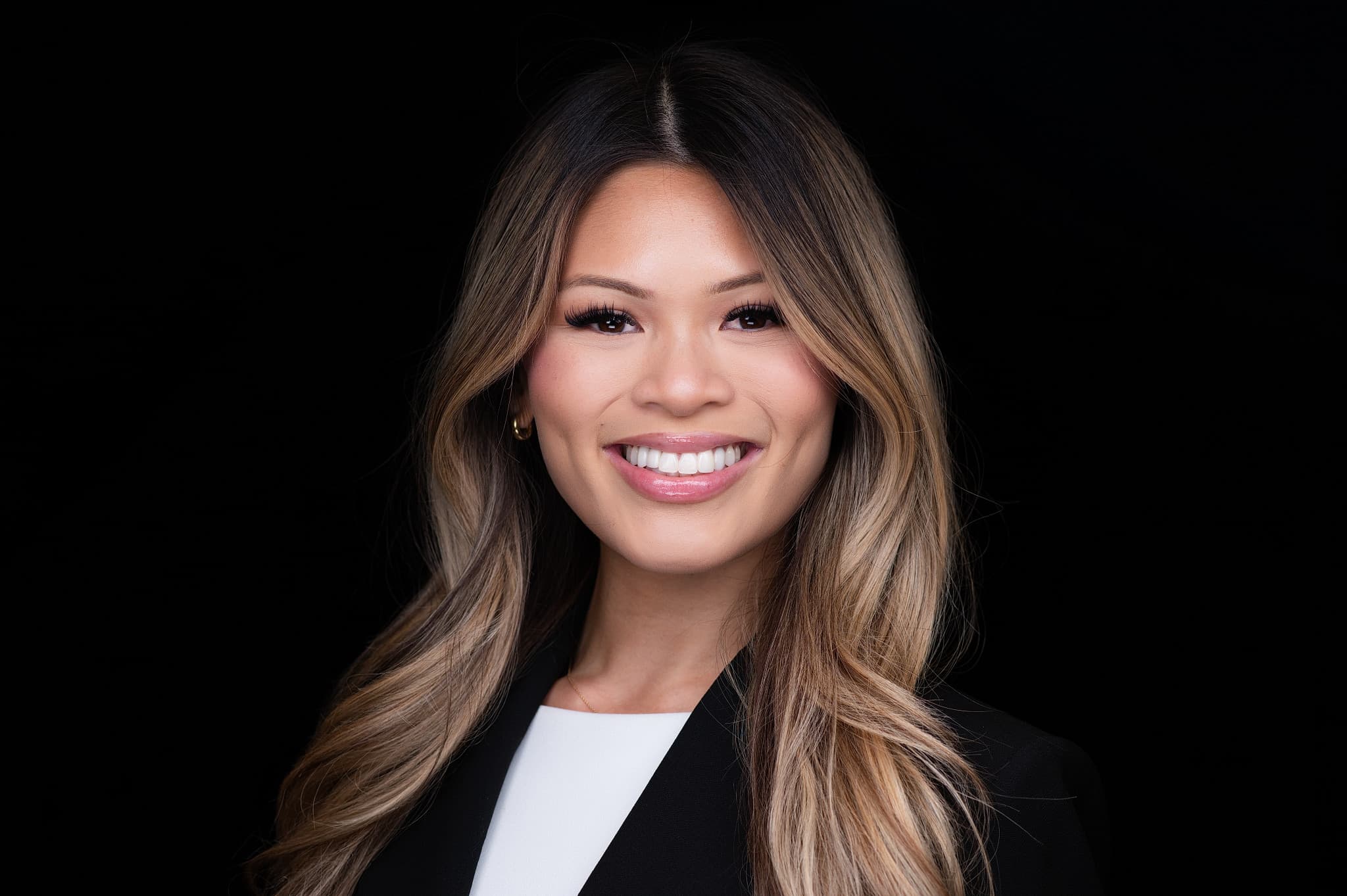 Approachable female professional headshot with warm smile, dark hair with highlights, black blazer