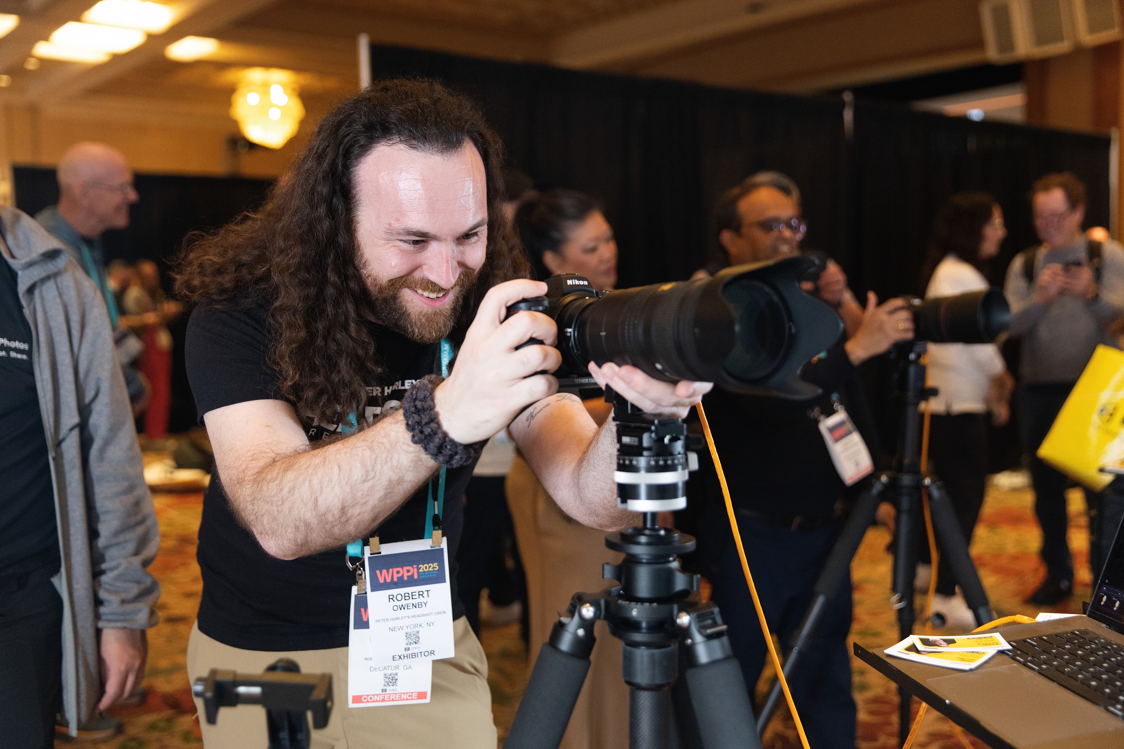 Robert Owenby photographer setting up professional camera at WPPI 2025 conference headshot booth with active attendee traffic