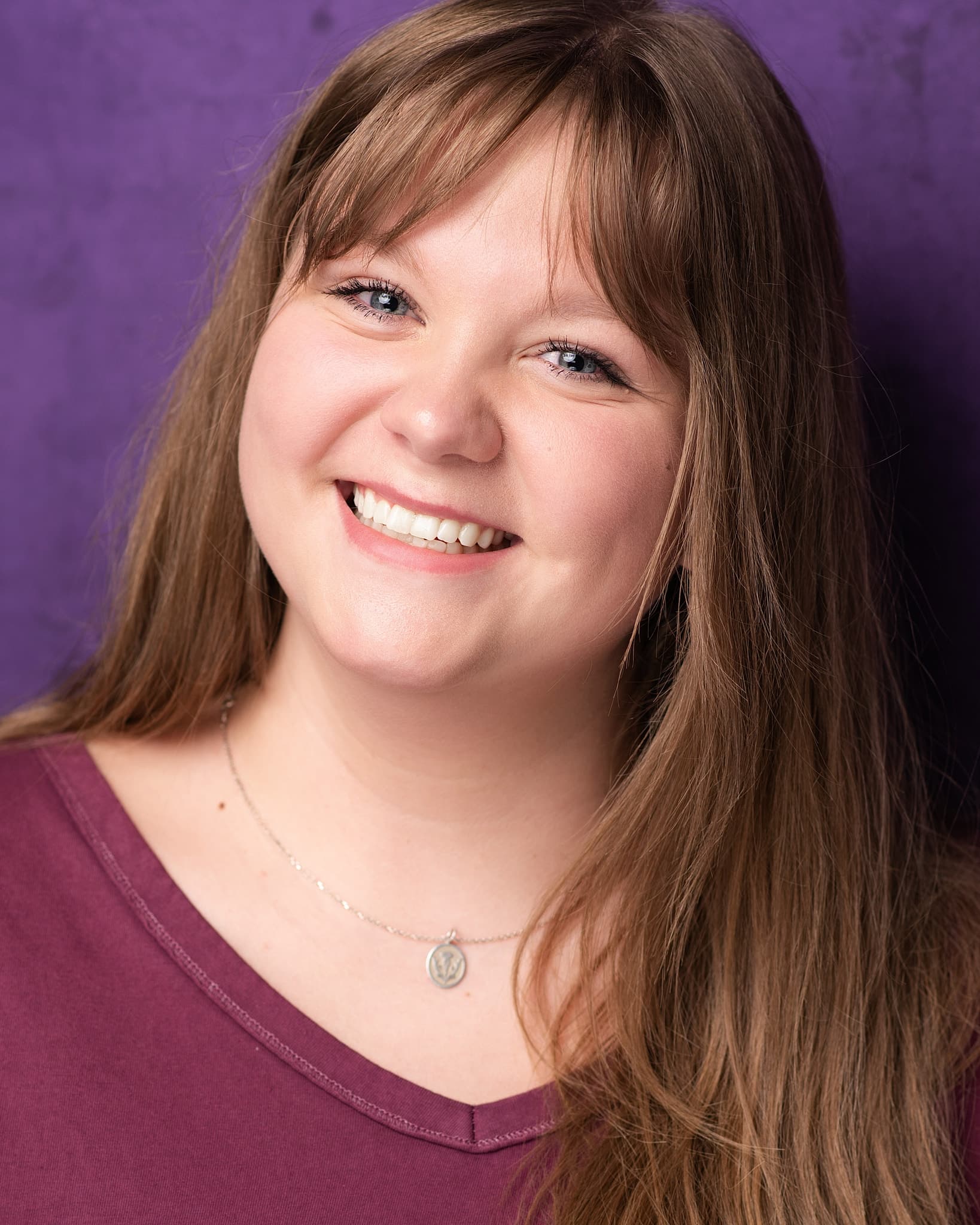 Atlanta commercial actor headshot of Caroline Neal, woman with long brown hair and a warm smile in a burgundy top against a purple backdrop