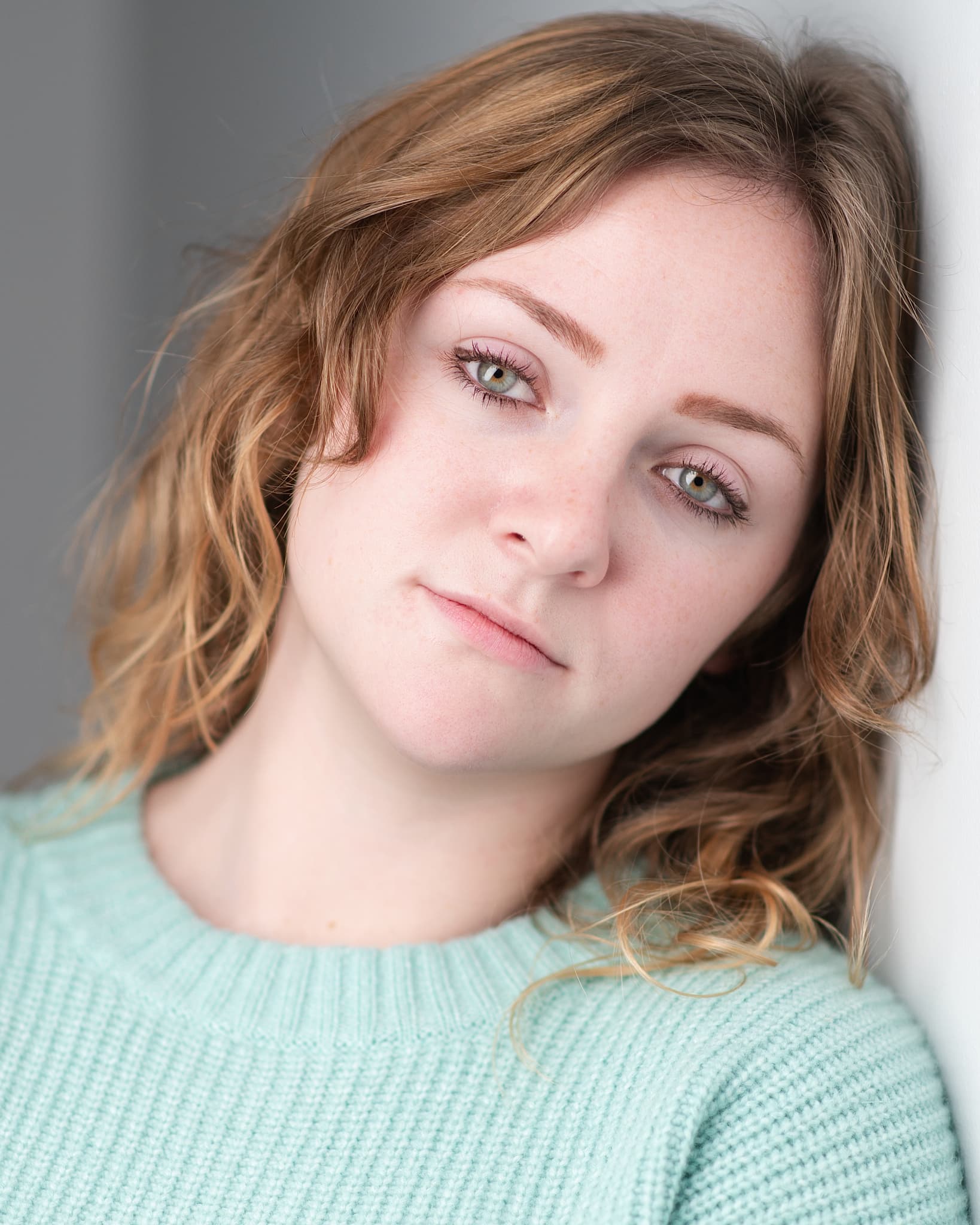 Atlanta actor headshot of Ginger Williams, young woman with wavy auburn hair and green eyes in a mint sweater against a soft gray background