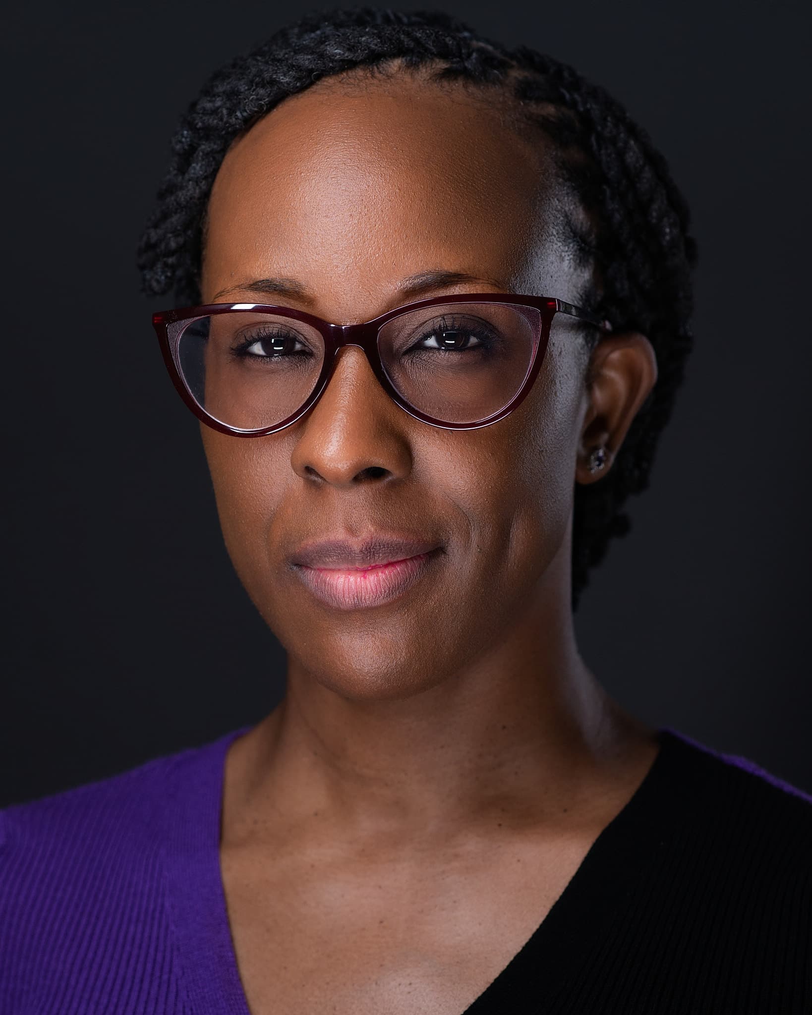 Atlanta theatrical actor headshot of Veronica Tinsley, woman in burgundy cat-eye glasses and a purple top with a composed expression against a dark background