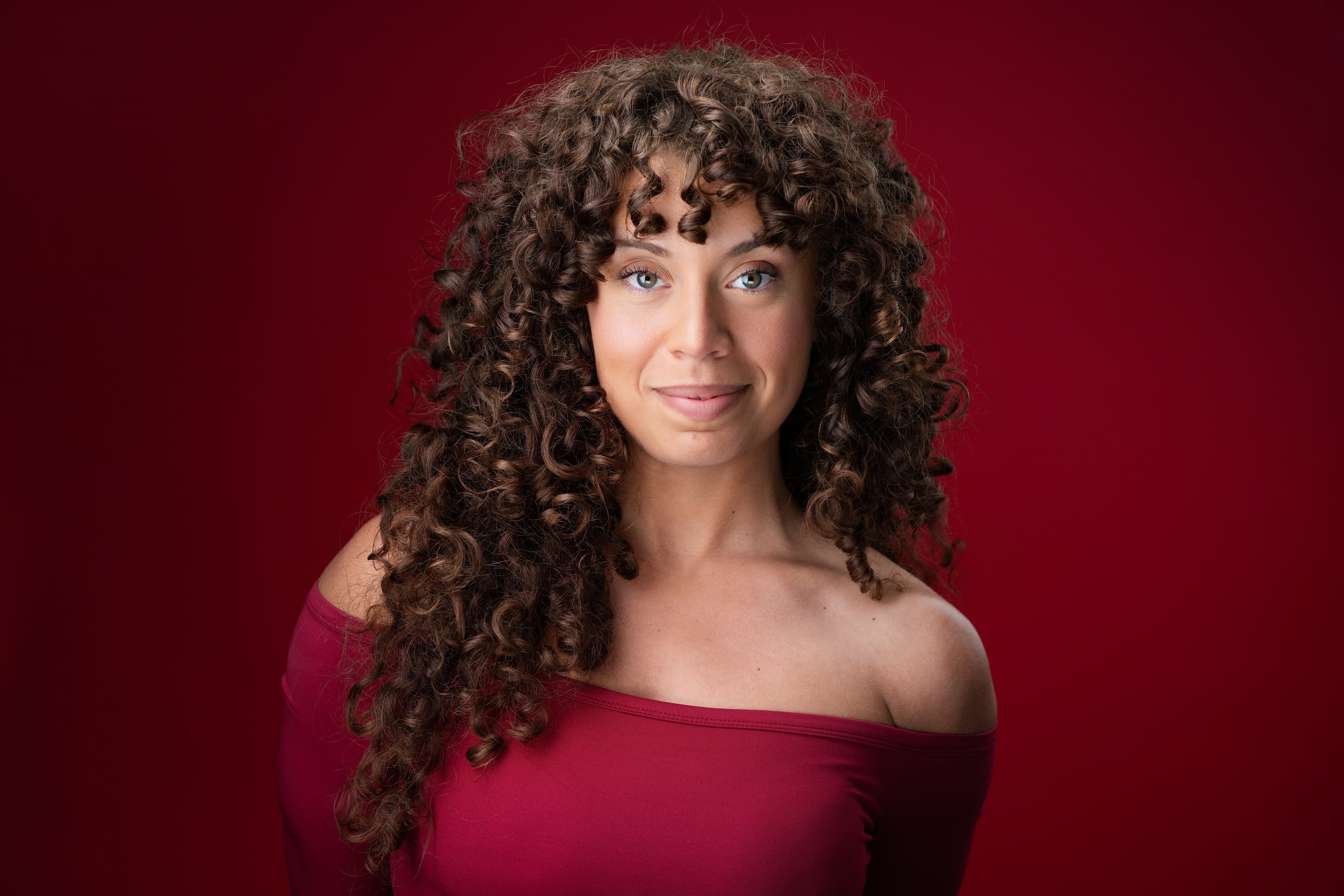 Atlanta actress headshot with curly hair in off-shoulder top against deep red backdrop