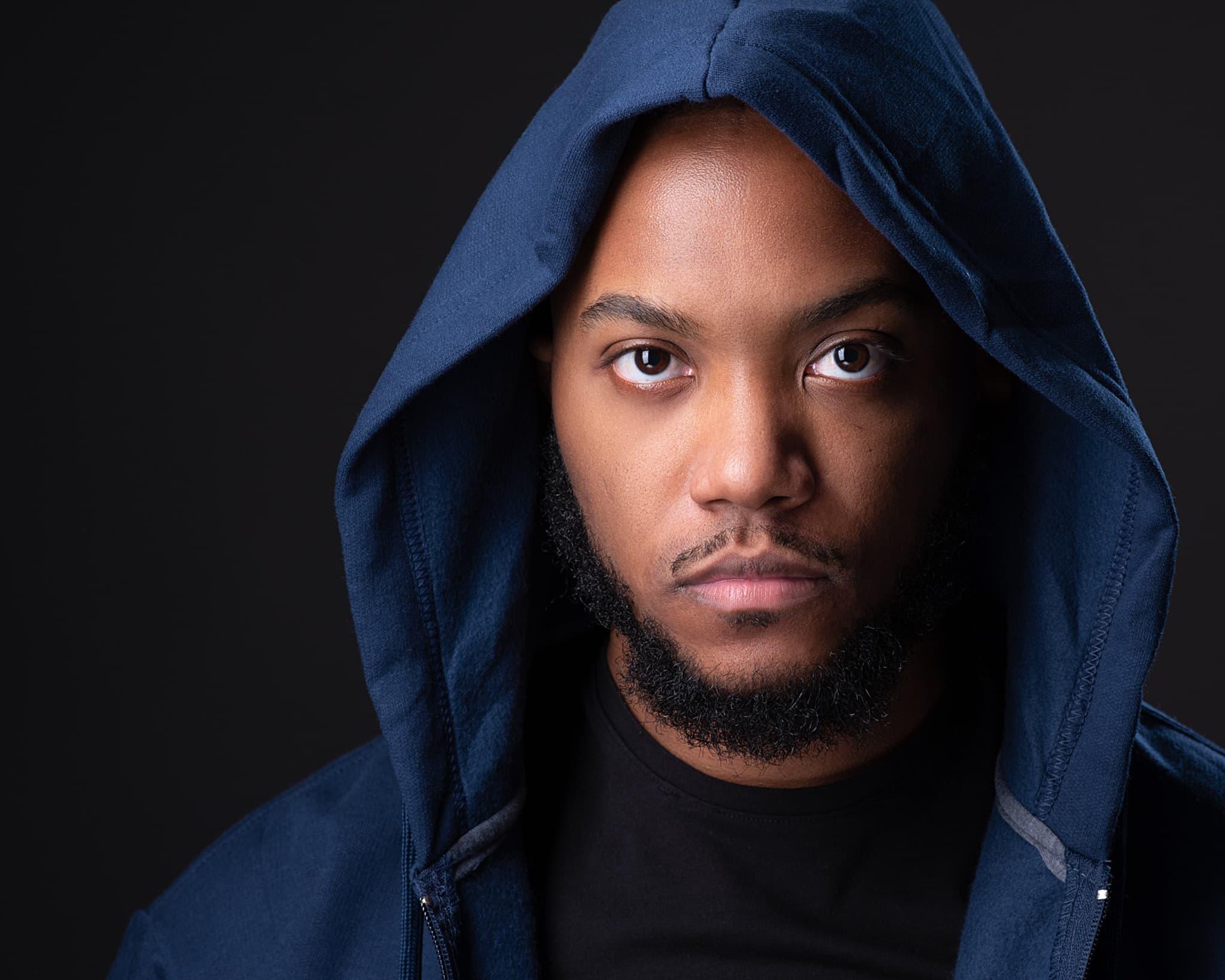 Dramatic actor headshot of man in hooded jacket with moody studio lighting