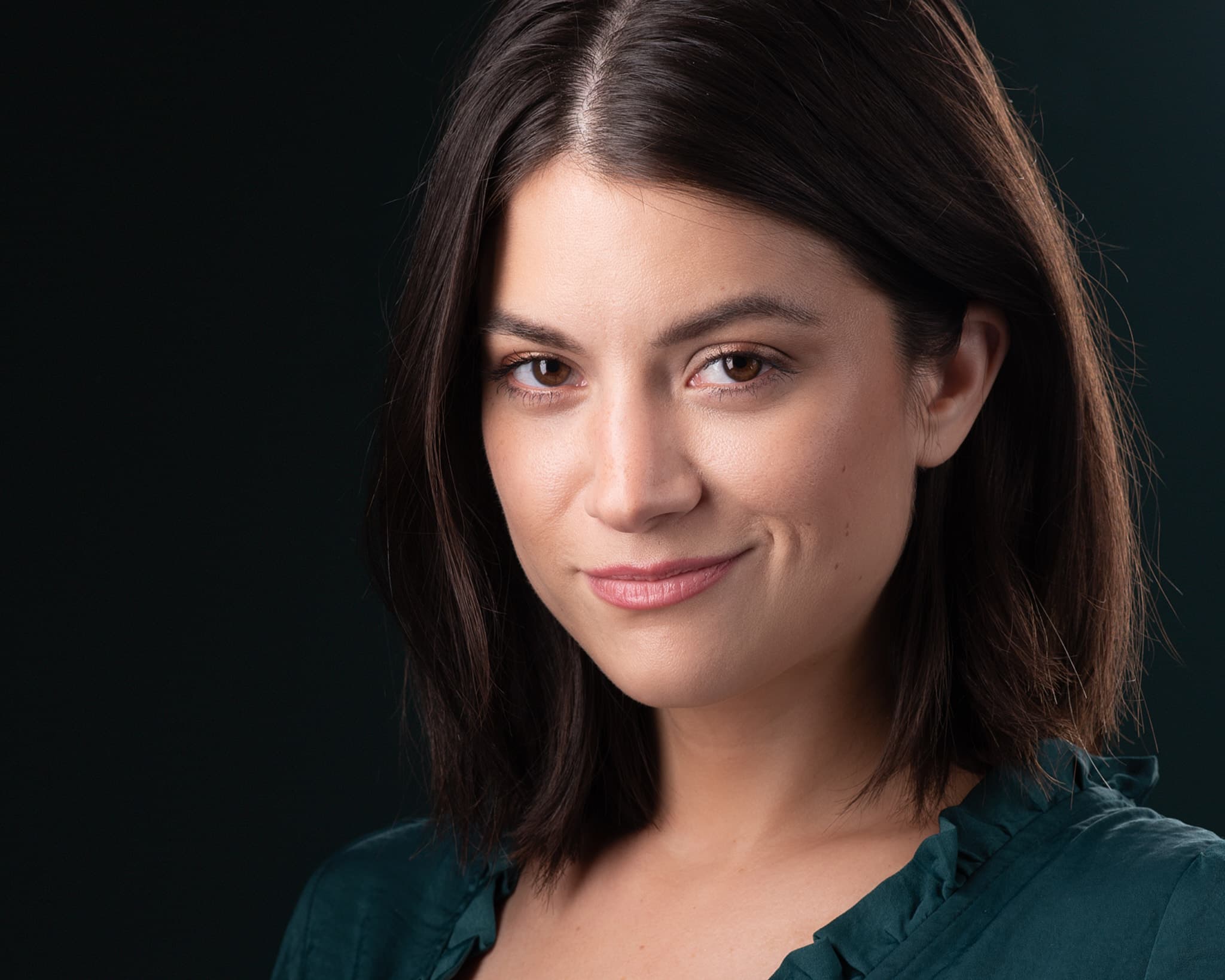Theatrical headshot of actress in green blouse with subtle expression and dark backdrop
