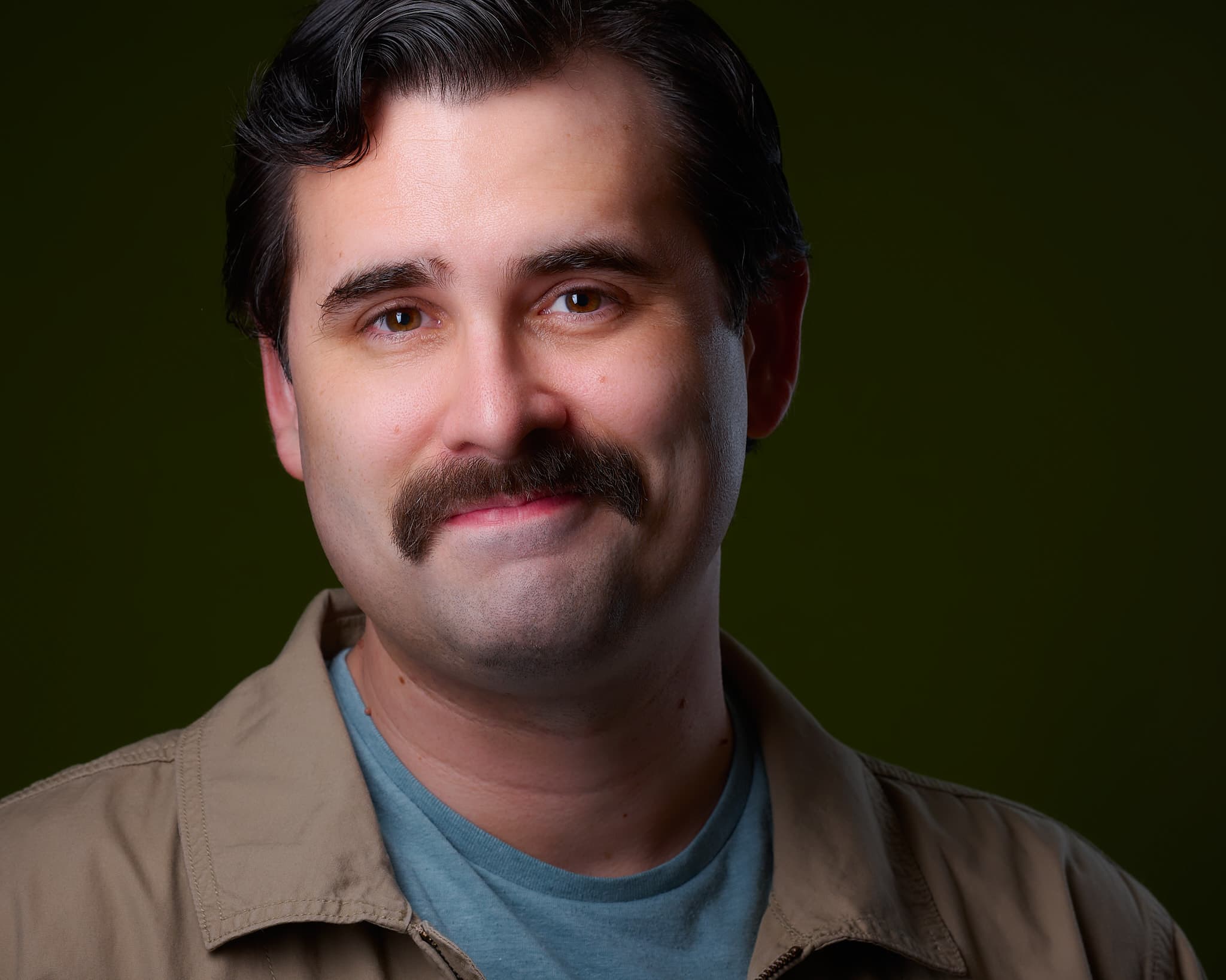 Character actor headshot of man in tan jacket with olive green studio backdrop
