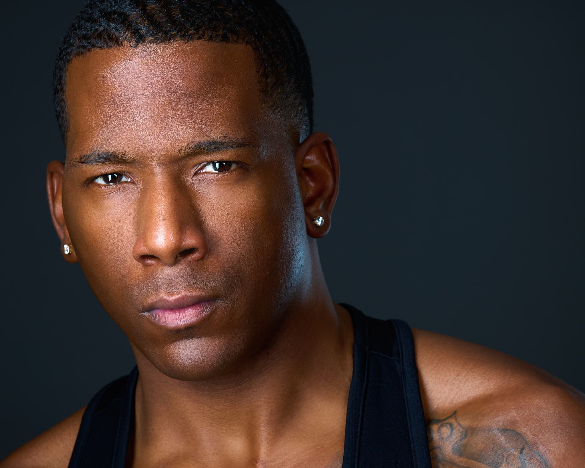 Intense theatrical headshot of actor in black tank top with dramatic studio lighting