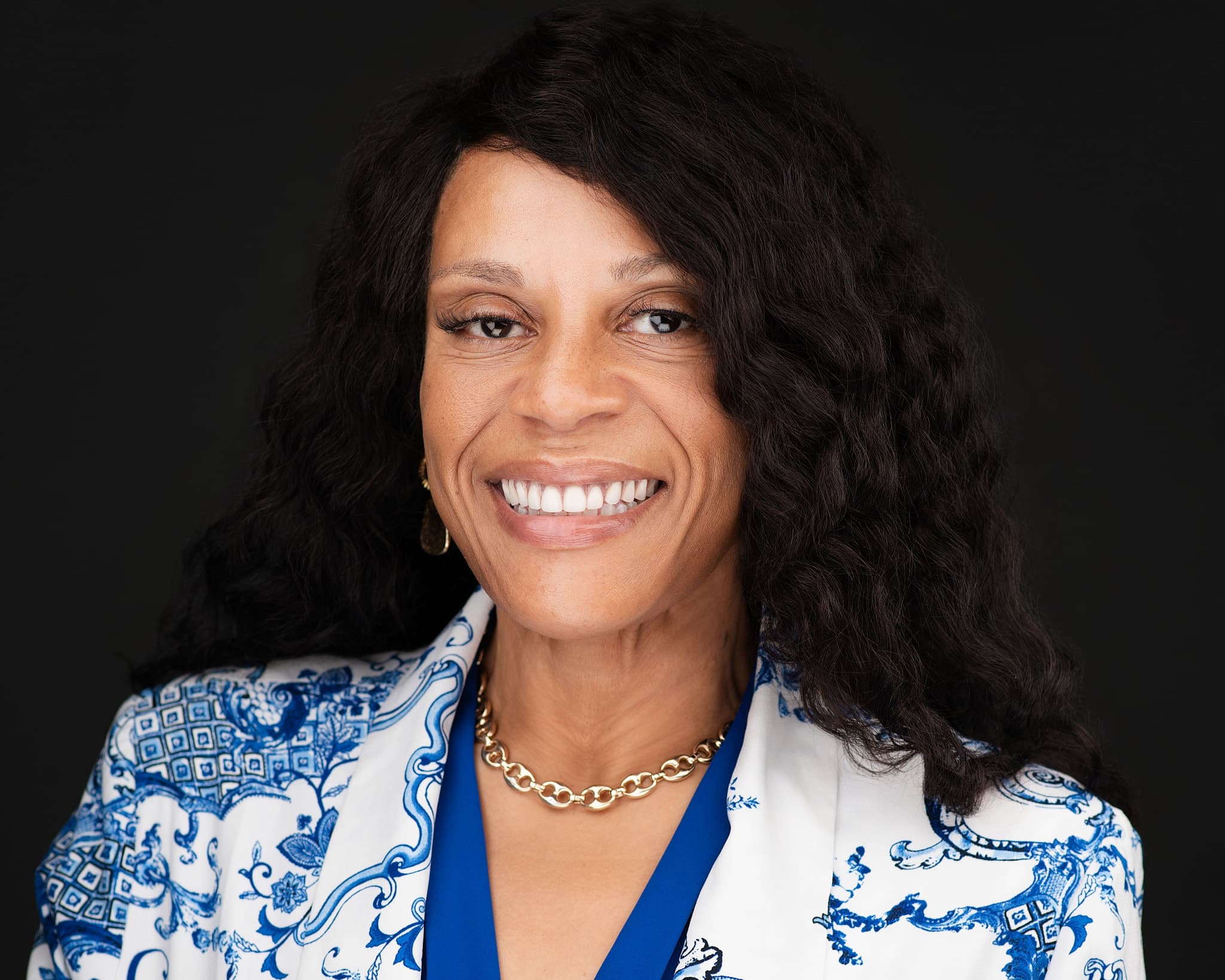 Executive woman's headshot with radiant smile in blue and white patterned blazer against deep blue background