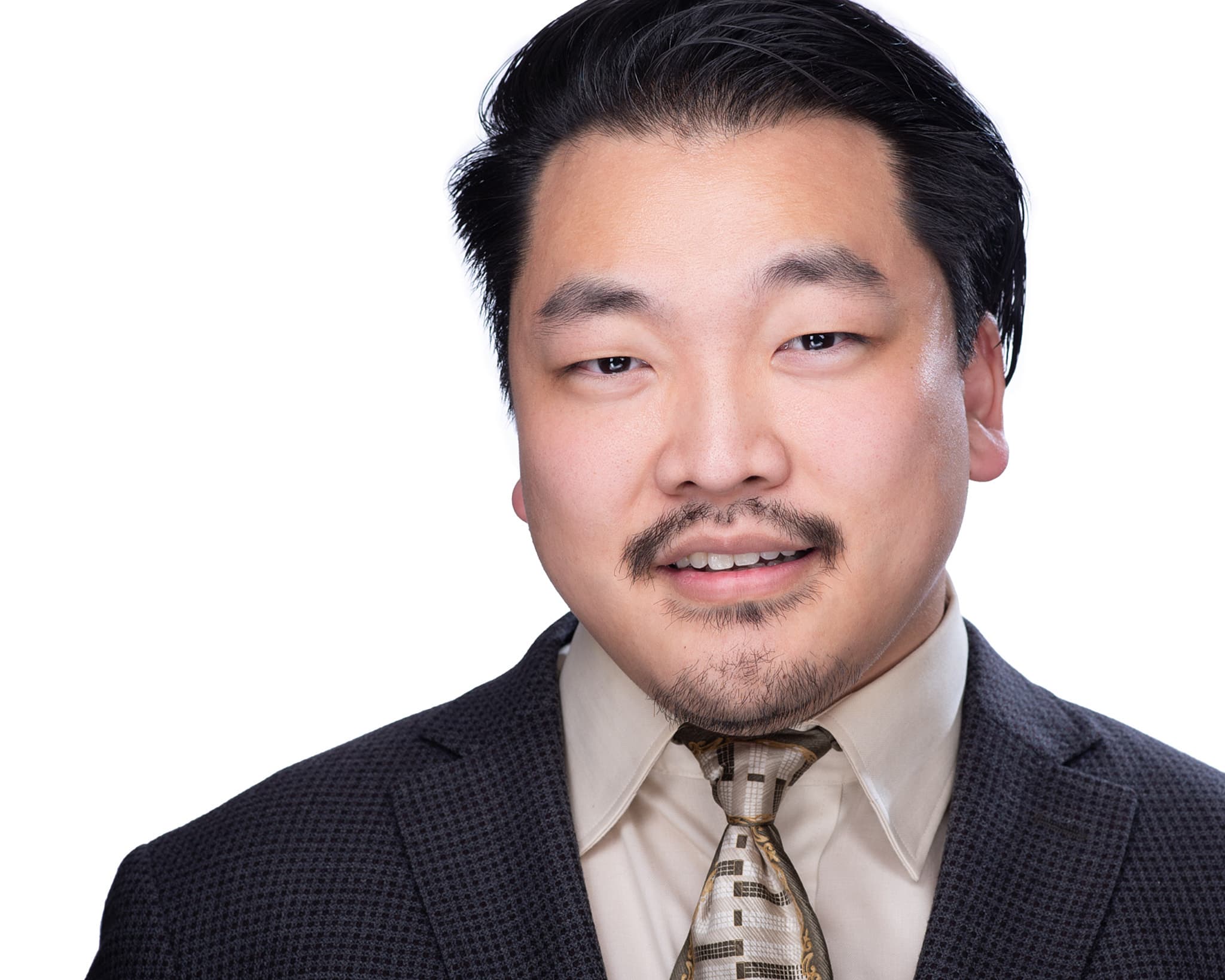 Professional headshot of man in charcoal suit and plaid tie on white backdrop