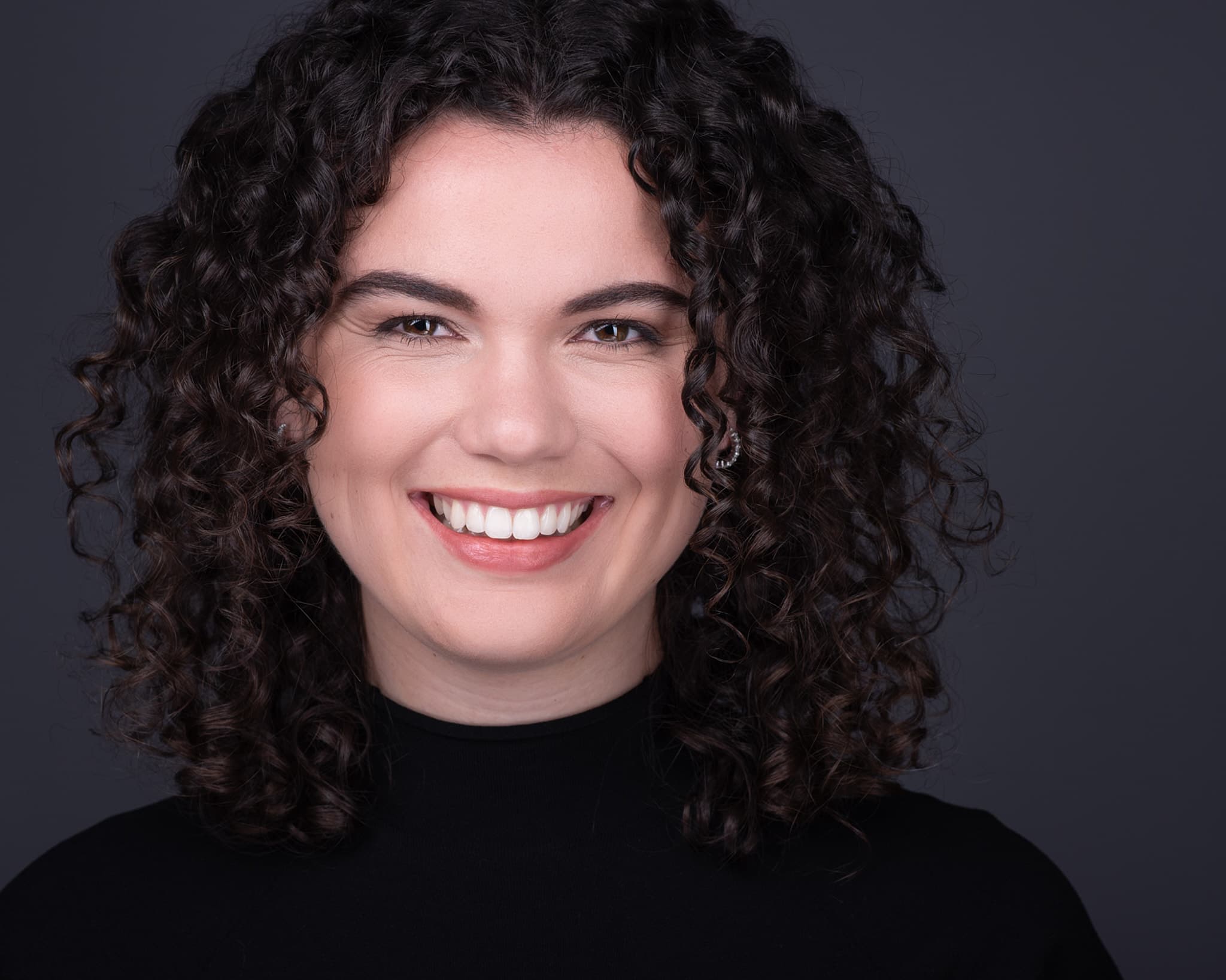 Professional portrait of woman with curly hair in black turtleneck on dark background