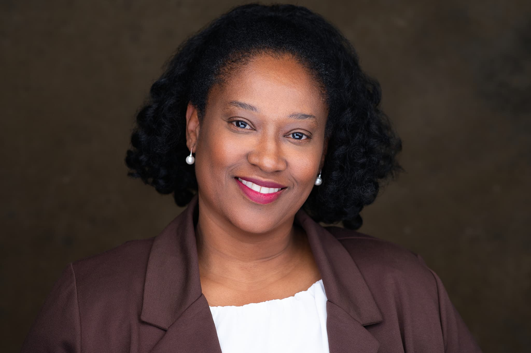 Experienced entrepreneur's headshot with warm smile, burgundy blazer, pearl earrings, radiant confident expression professional studio