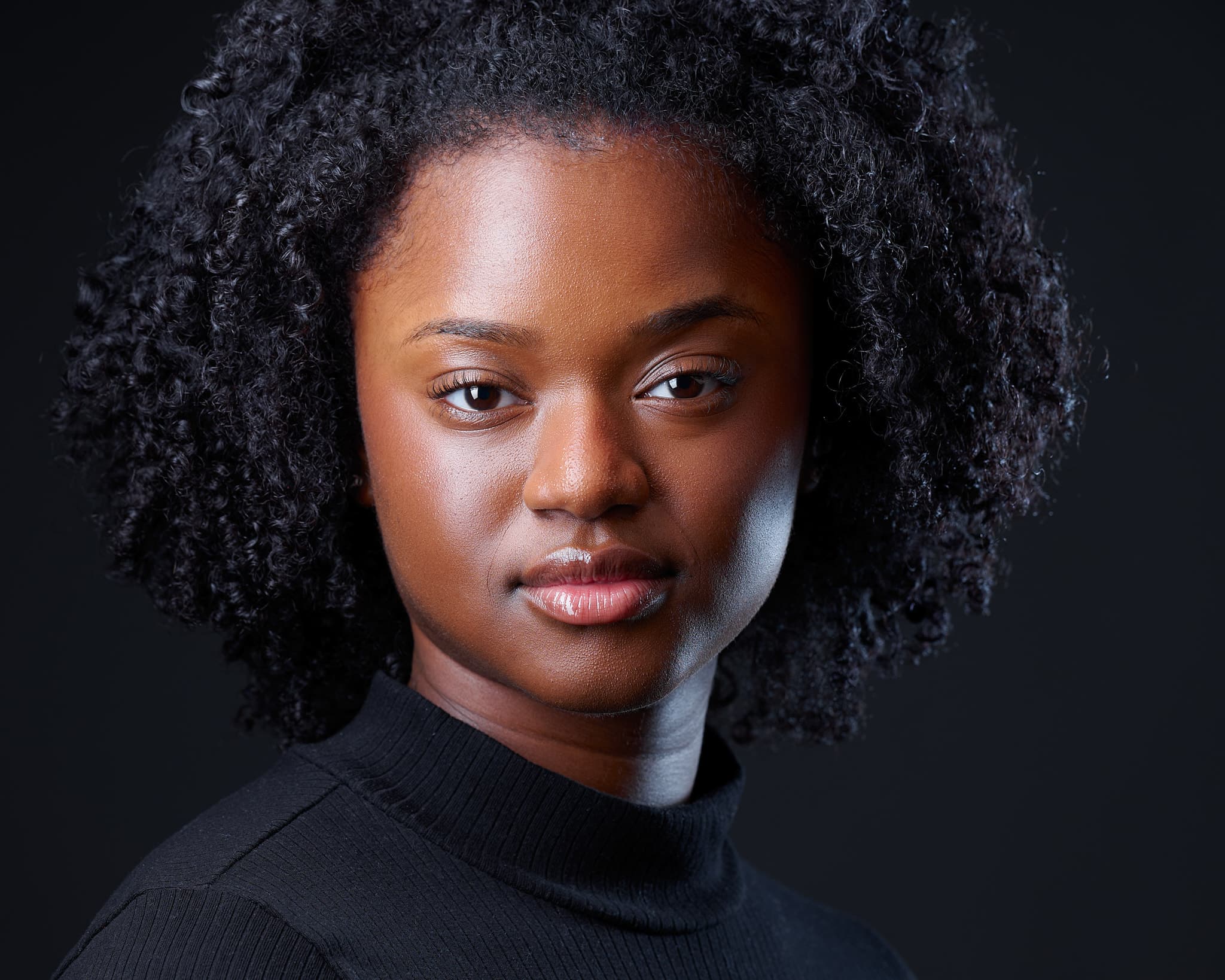 Atlanta theatrical actor headshot of Neija LeBrun, woman with coiled black curly hair in black turtleneck against dark charcoal background