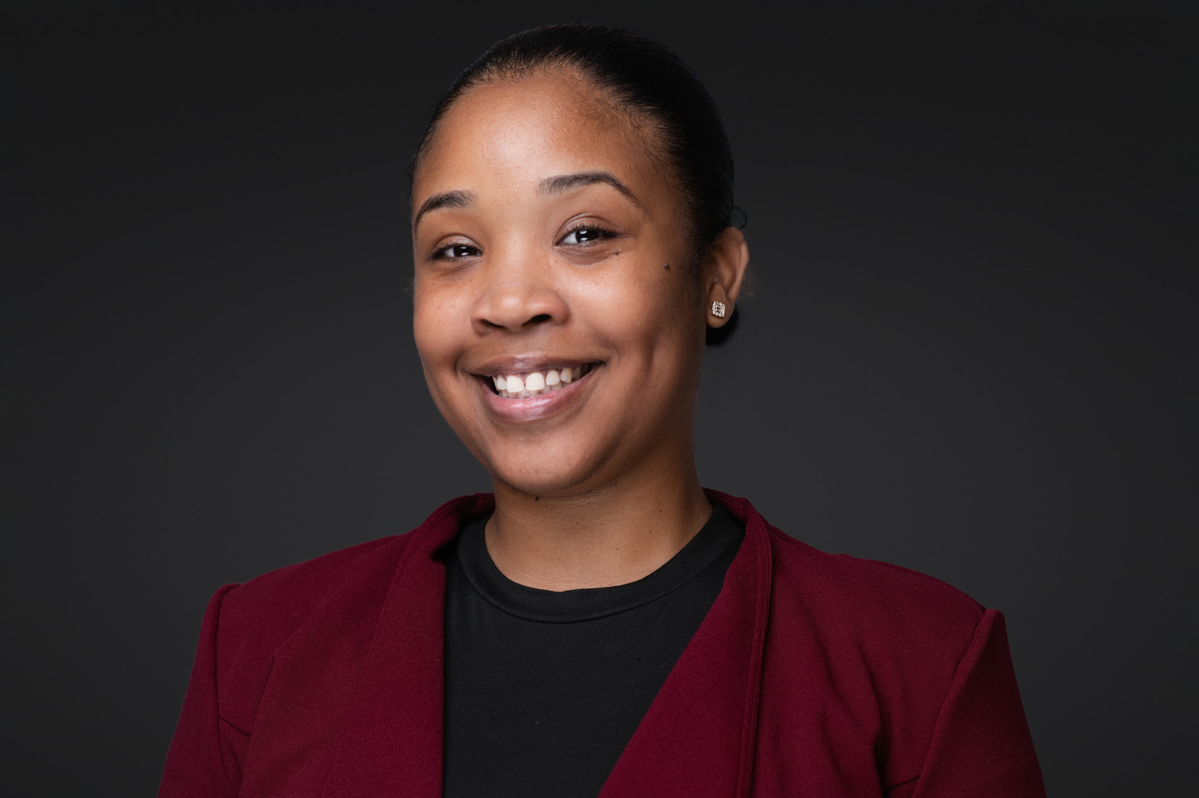Professional headshot of woman in burgundy blazer with sleek updo, bright smile, and confident warm expression