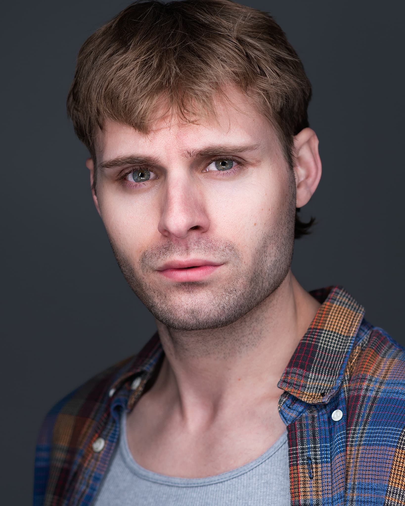 Atlanta actor headshot of Trace Collie, young man with tousled blond hair and blue eyes in a layered plaid flannel against a gray studio background
